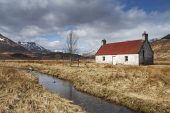 Ancient croft in rough grassland to the west of Loch Affric with snow covered mountains beyond and a stream in the foreground Glen Affric National Nature Reserve Highland Region Scotland UK April 2015